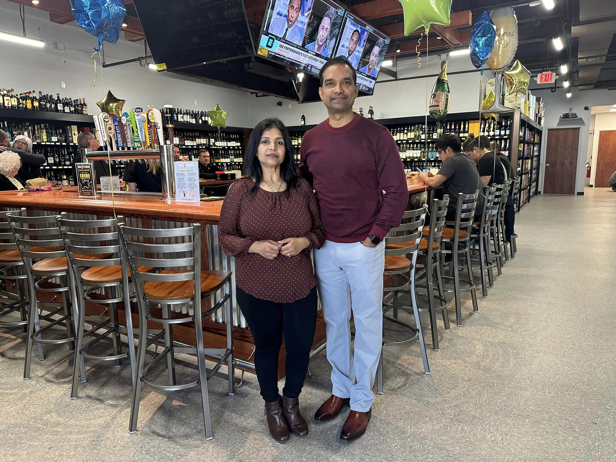 Business owners standing in front of bar with high top chairs with customers in the background