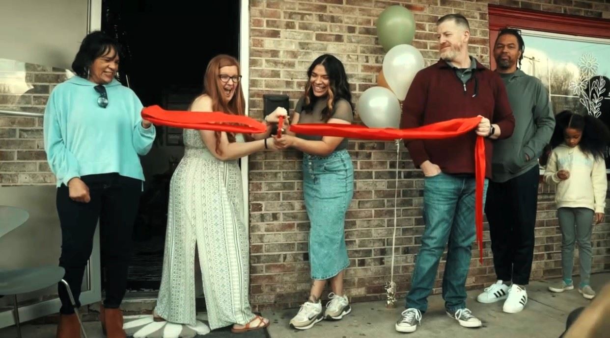 Individuals cutting a red ribbon outside of the Healing House facility