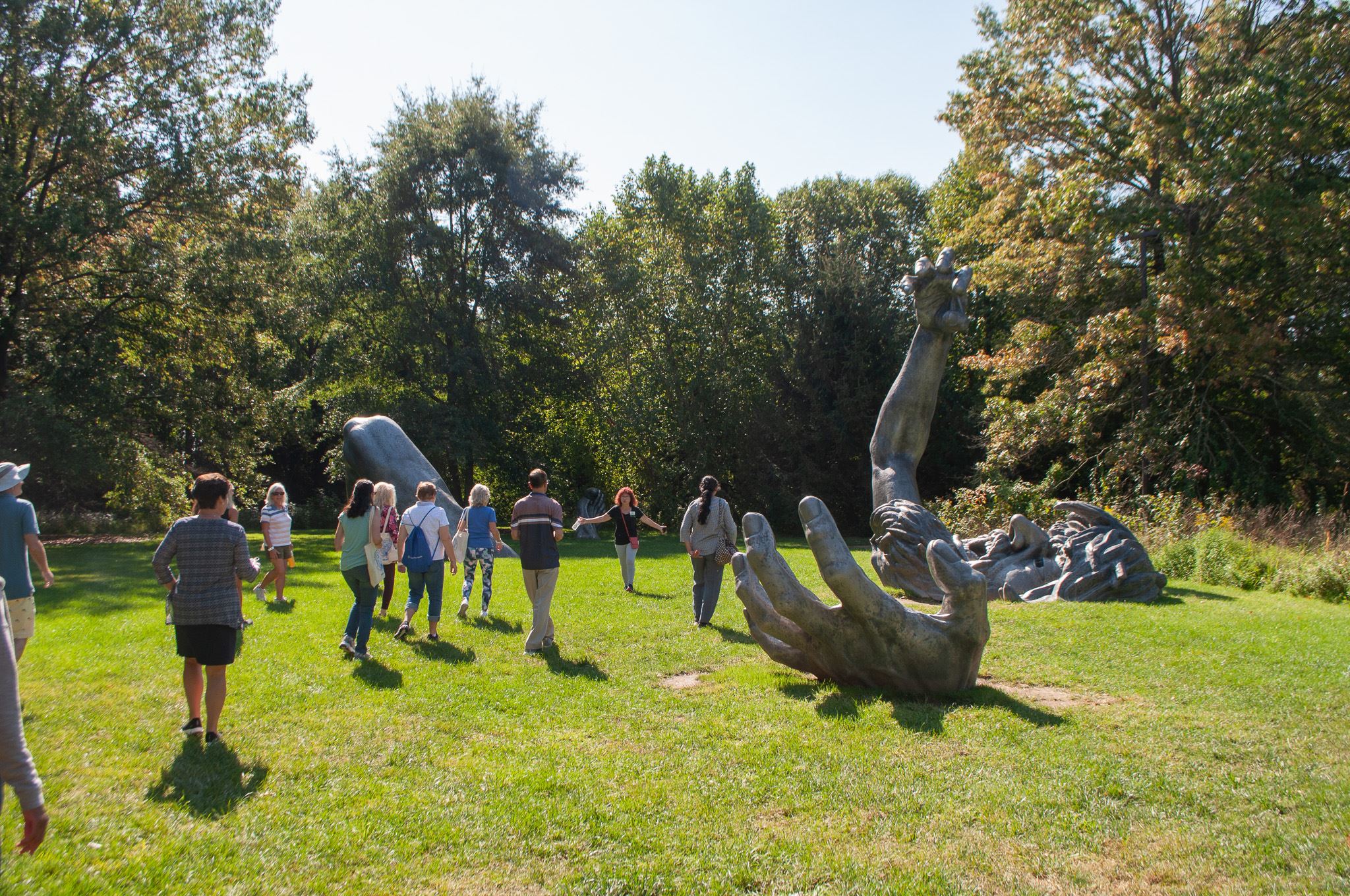 Group of people walking around statue with hands coming out from ground